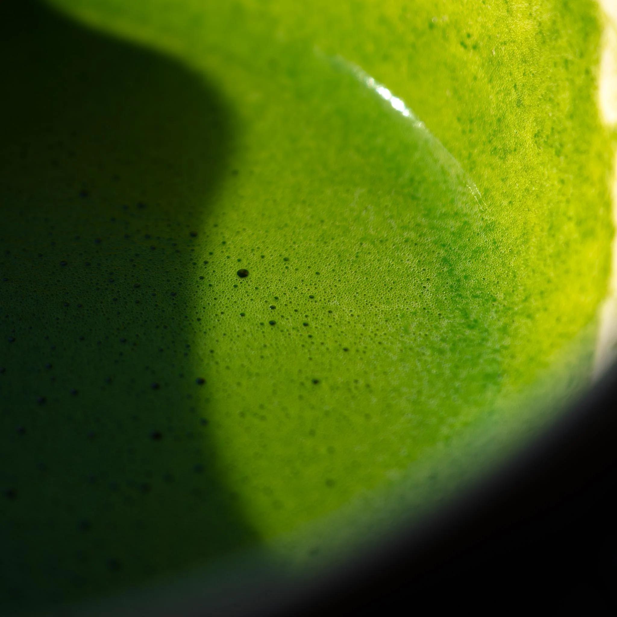 A close-up shot of vibrant green whisked matcha tea with fine foam in a traditional bowl.