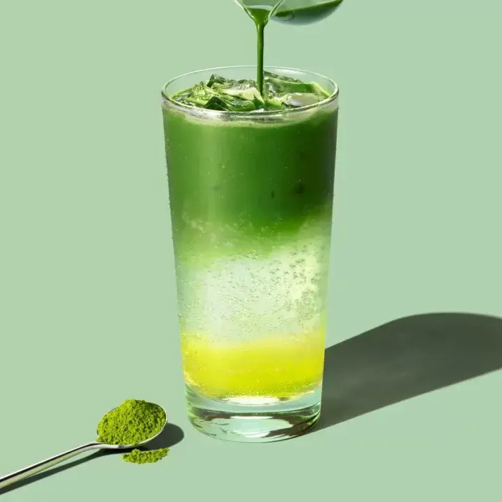 Layered iced sparkling citrus matcha beverage in a tall glass with ice cubes, showing a bright green matcha top layer, effervescent middle layer, and yellow citrus base.