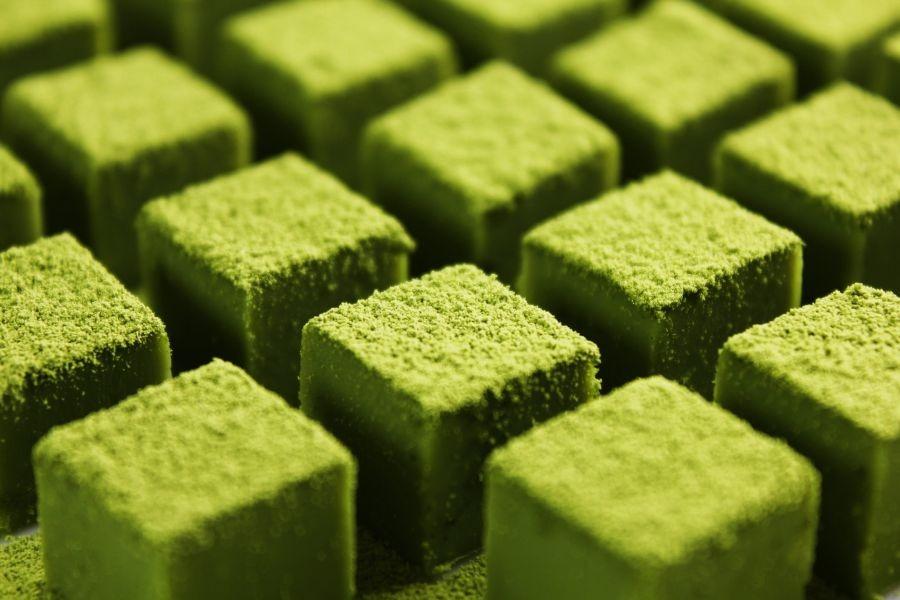 Square green matcha chocolates dusted with micro-fine matcha powder arranged in rows.